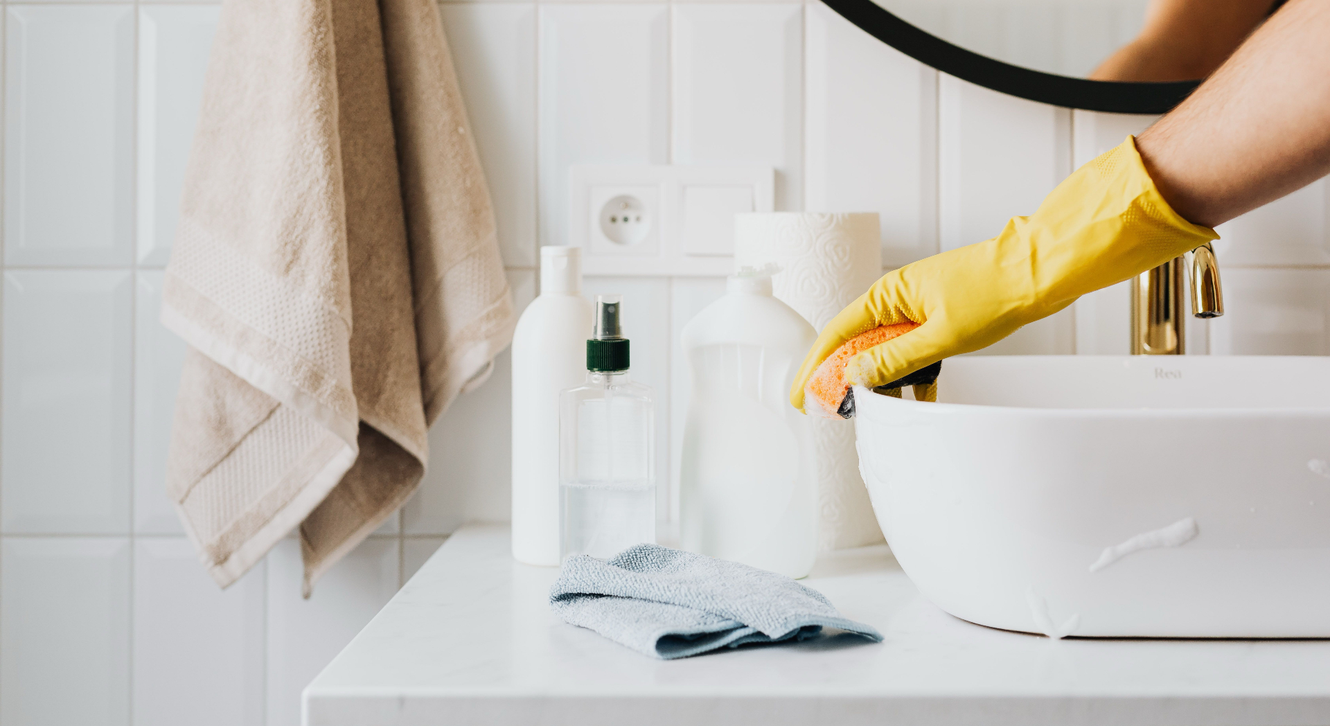 Gloved hand cleaning a bright modern bathroom sink with supplies