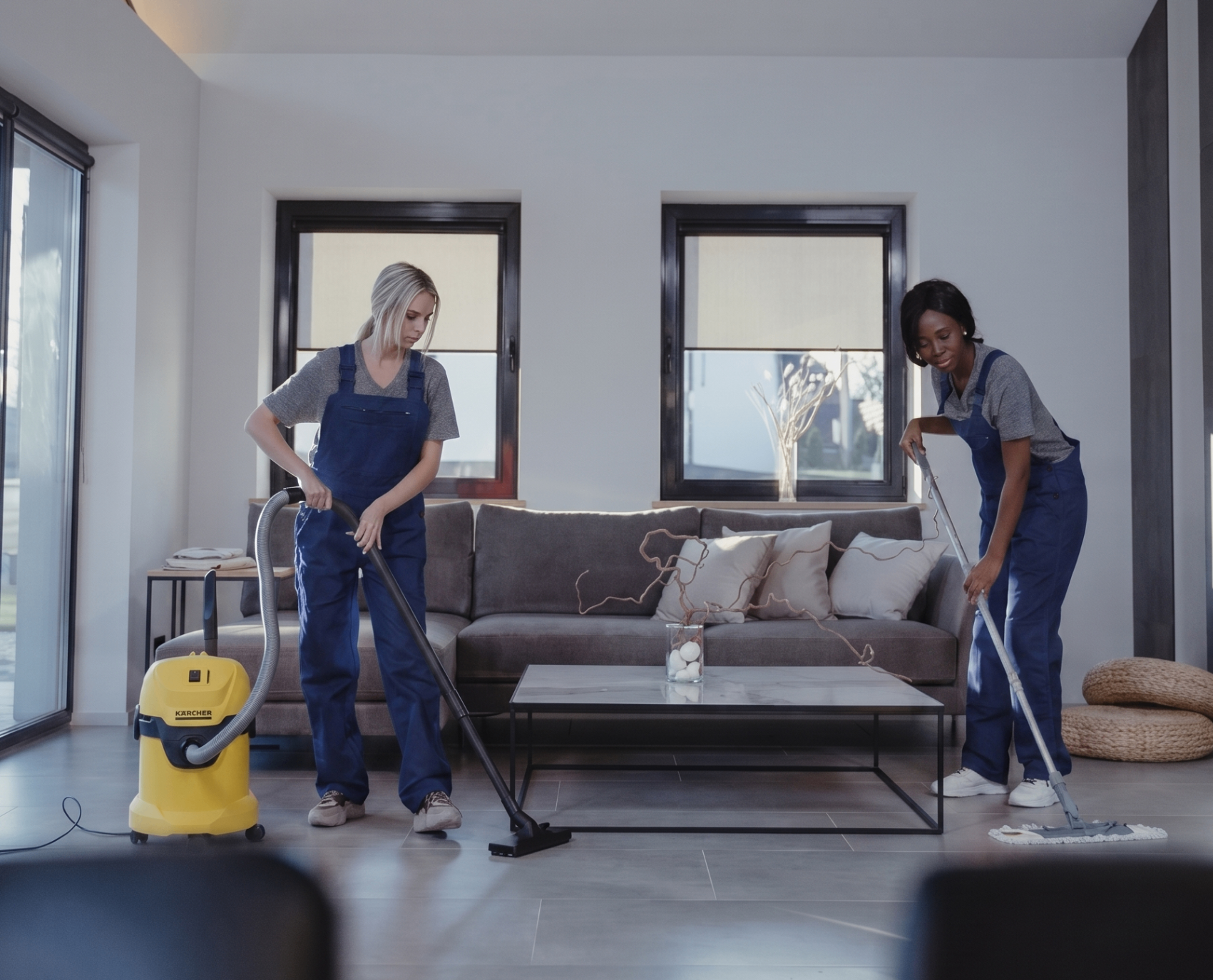 Two professional cleaners working together to vacuum and mop a modern living room
