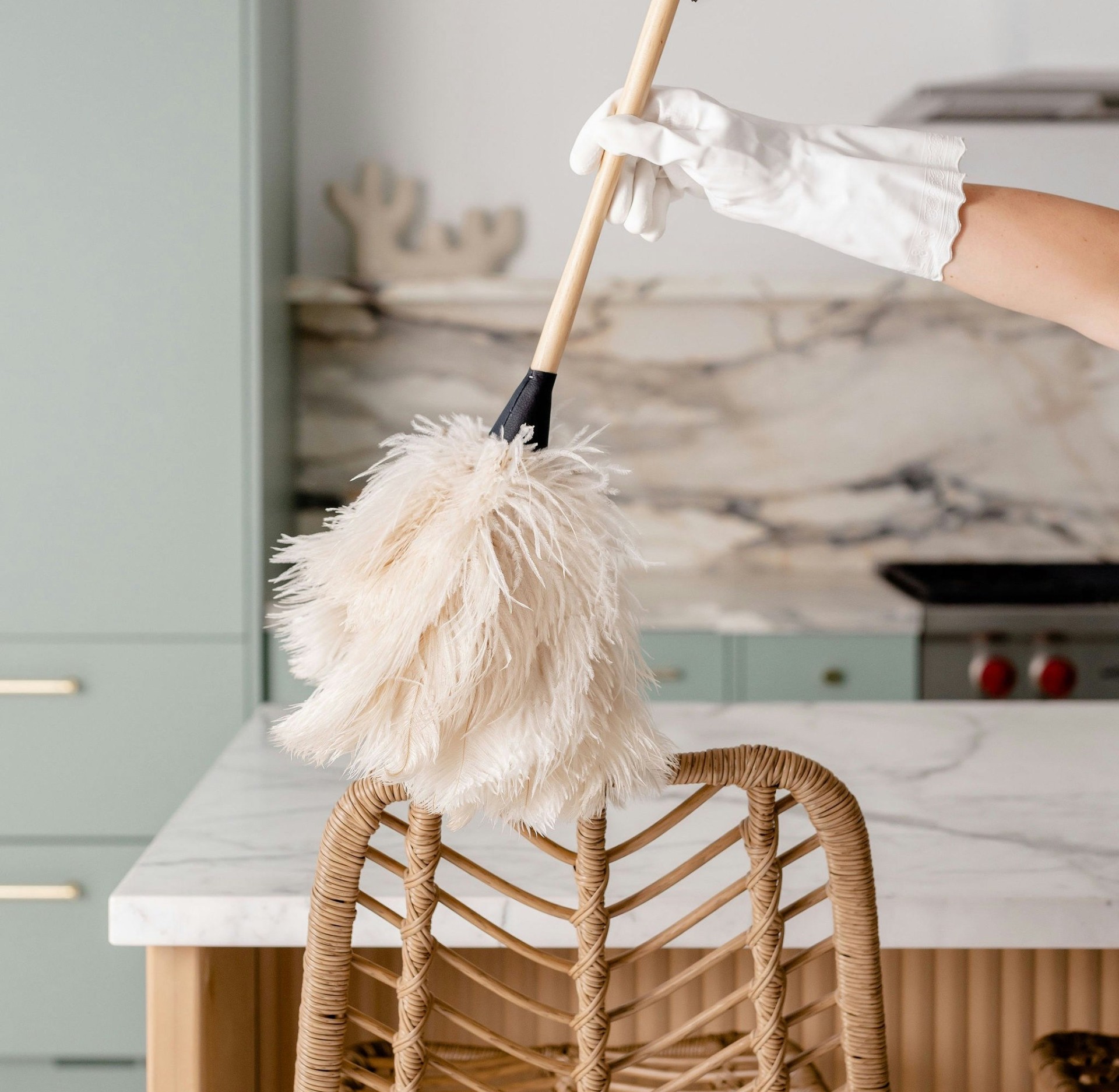 Gloved hand dusting a bright marble kitchen with a feather duster