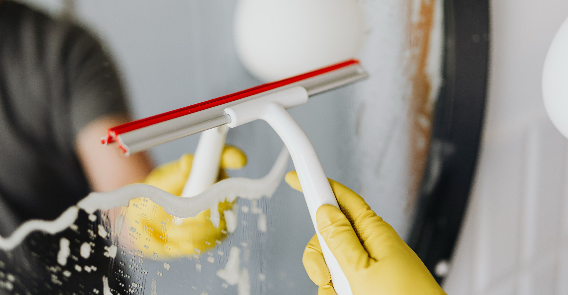 Gloved hand using a squeegee to clean a bathroom mirror
