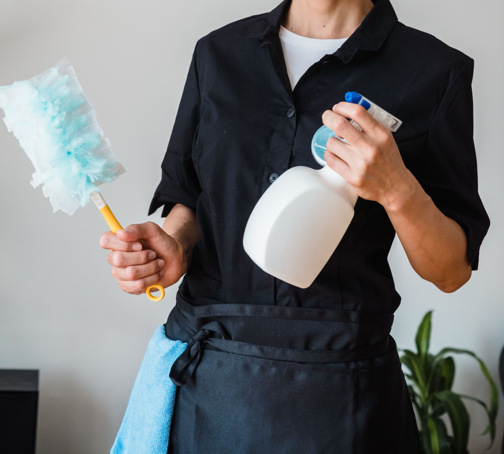 Professional cleaner in a black uniform holding a duster and spray bottle