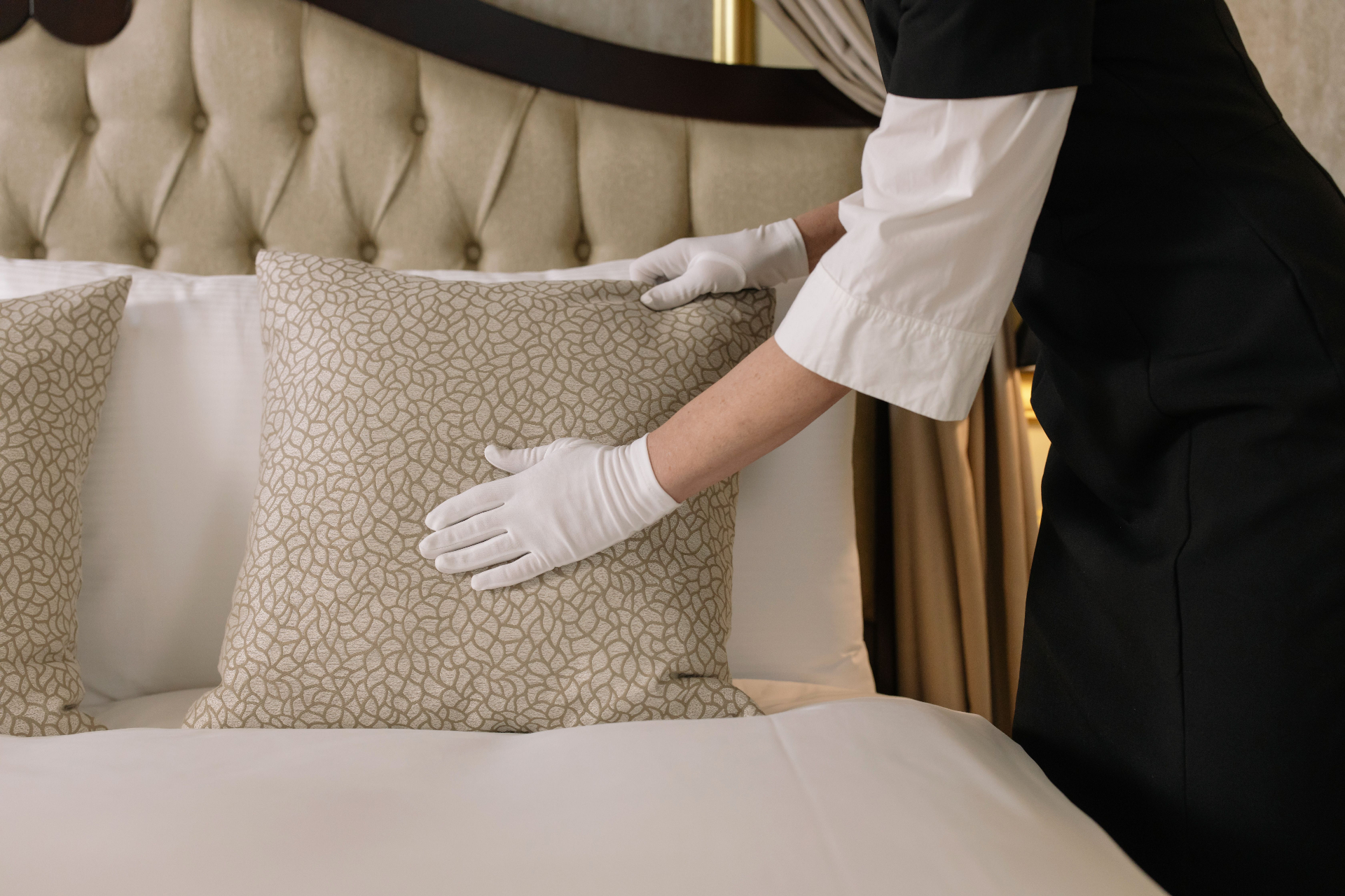Professional cleaner in white gloves arranging pillows on a freshly made bed in a vacation rental